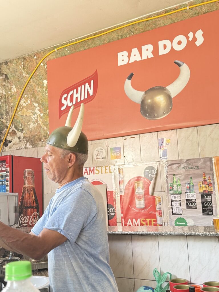 Nelson, dono do Bar do Corno, usando capacete de viking com chifres atrás do balcão