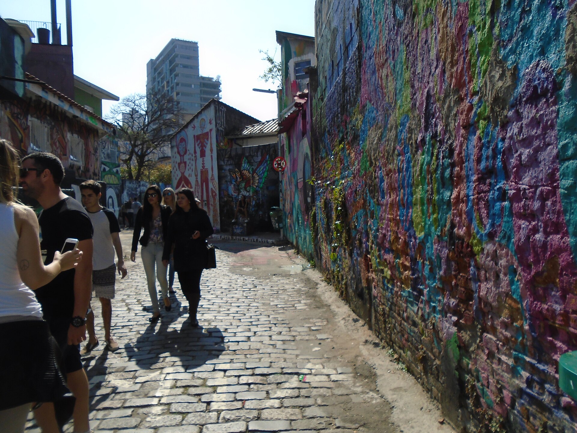 Turistas caminhando e fotografando no Beco do Batman em dia de sol
