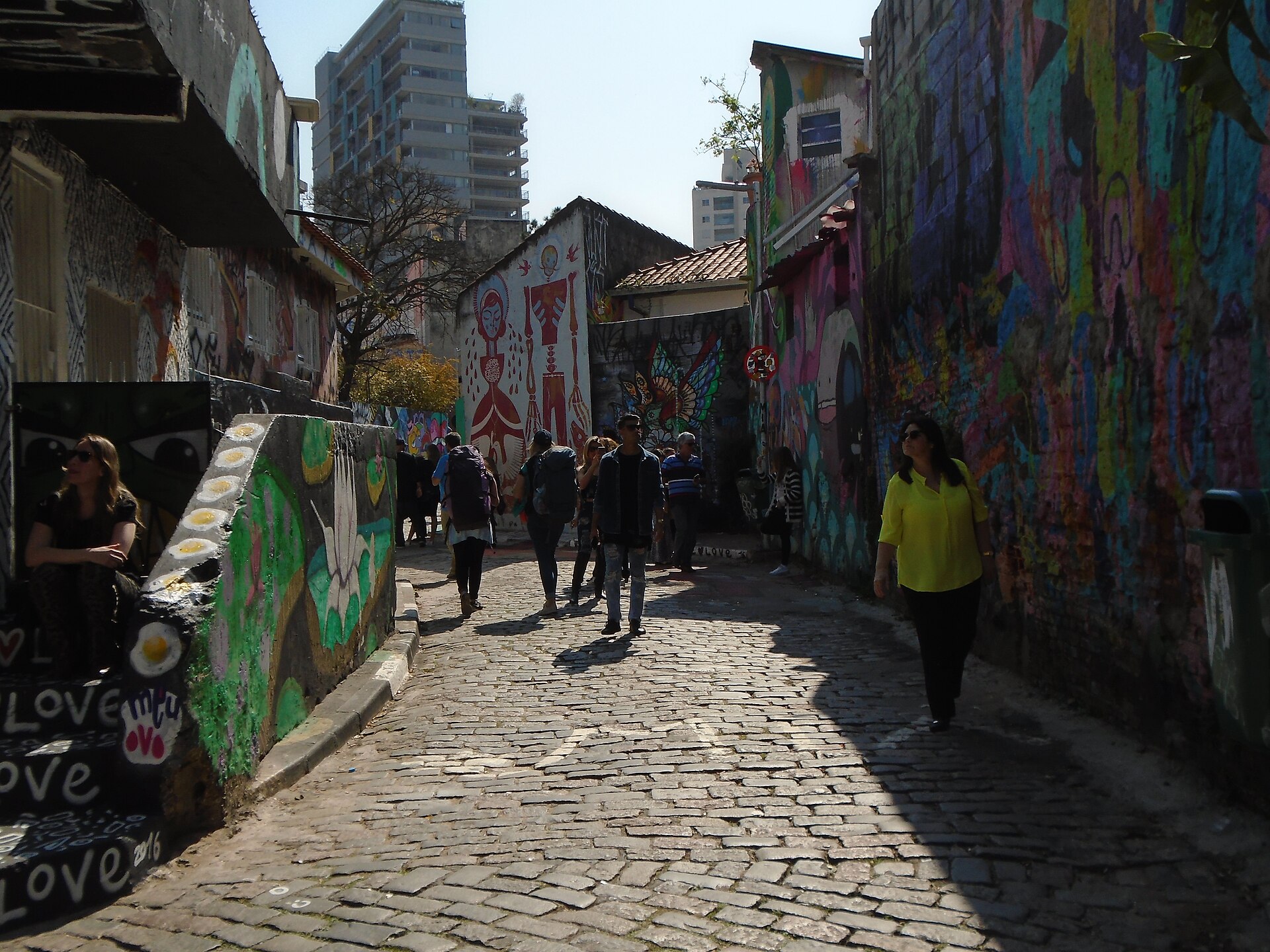 Visitantes caminhando pela viela de paralelepípedos do Beco do Batman entre muros grafitados