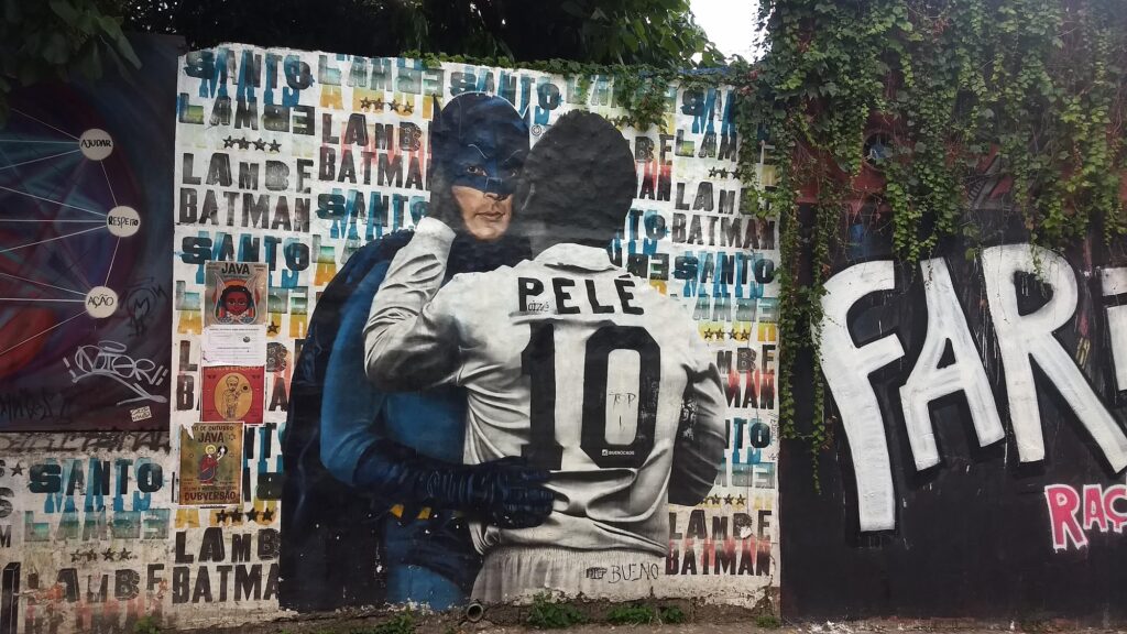 Grafite do Batman abraçando Pelé de costas, com a camisa número 10, em muro do Beco do Batman
