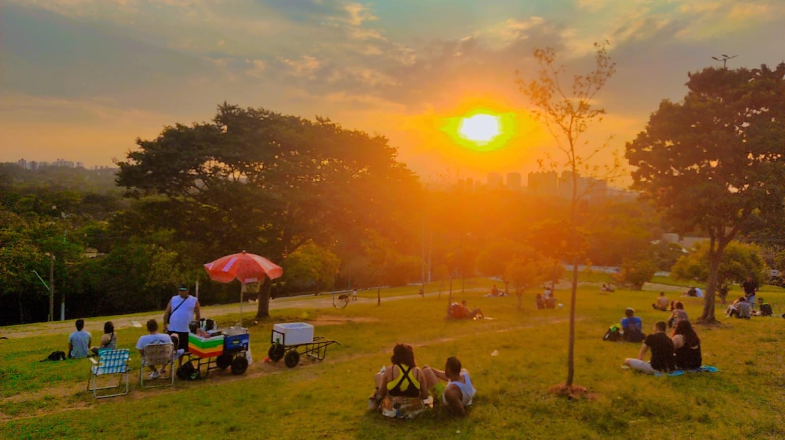 Pessoas sentadas no gramado da Praça Pôr do Sol ao entardecer